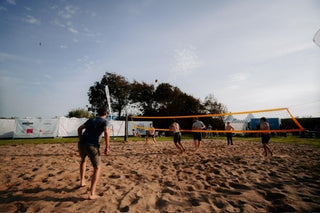 Männer die bei Sonnenschein Beachvolleyball auf dem Festivalgelände spielen.